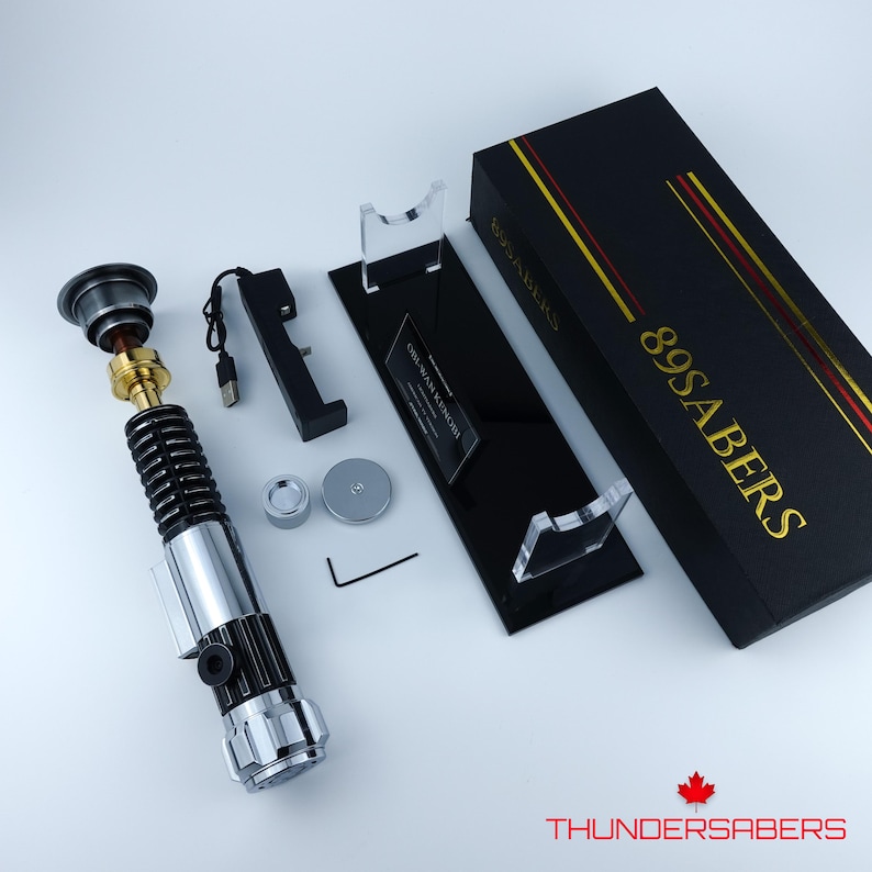 May include: A lightsaber prop with a silver, black, and gold finish, presented with a black display stand and a black box with gold lettering reading "89SABERS". Accessories include a charging cable and small metal components.