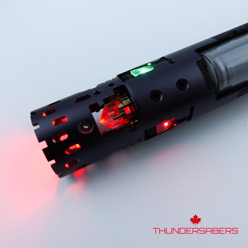 Puede incluir: Una empu&ntilde;adura de sable l&aacute;ser negra con luces internas rojas y verdes. La empu&ntilde;adura tiene un dise&ntilde;o detallado con cortes y una secci&oacute;n transparente. El texto "THUNDERSABERS" es visible en rojo.