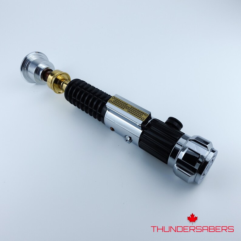 May include: A detailed lightsaber prop with a silver, black, and gold design. The hilt features a ribbed black grip, a silver midsection, and a gold and silver emitter. The end cap is chrome. The text "THUNDERSABERS" is at the bottom.