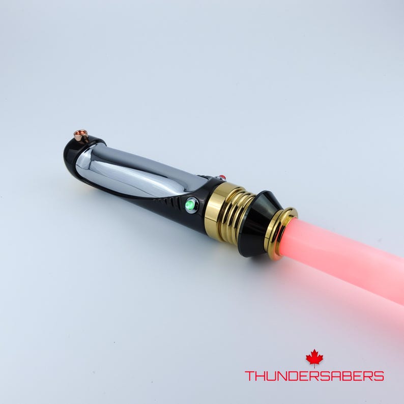 Puede incluir: Un sable de luz con una hoja rosa, un mango negro y detalles dorados y plateados. El mango tiene una empu&ntilde;adura negra y una secci&oacute;n plateada. El texto "THUNDERSABERS" es visible.