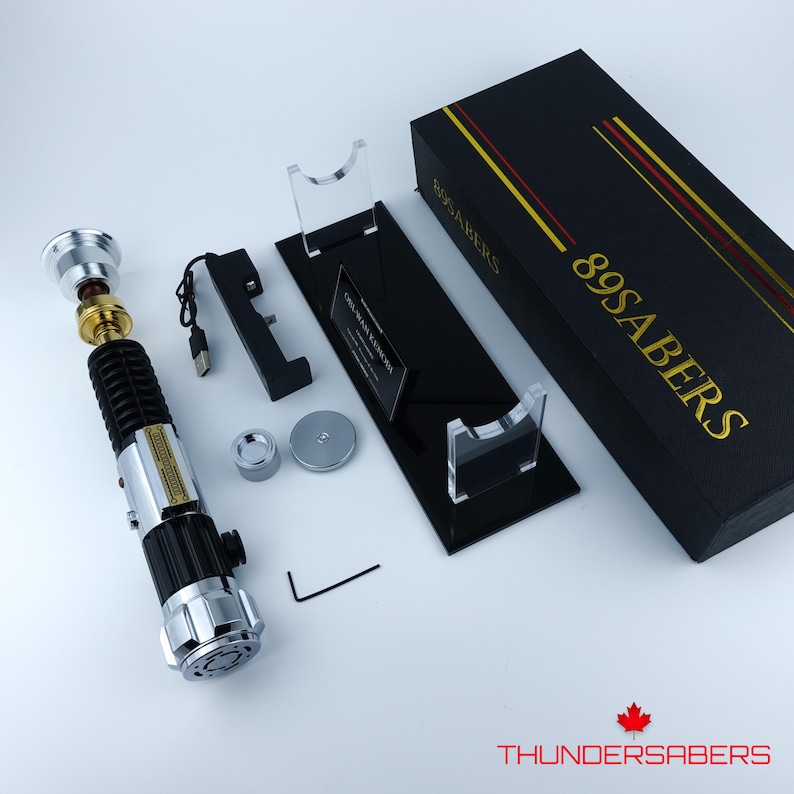 May include: A disassembled lightsaber with a black and silver handle, gold accents, and a silver top. Accessories include a black stand, a black box with gold lettering, and a small silver and black charging component. The box reads "89SABERS".
