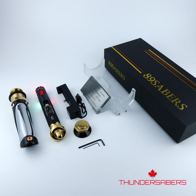 Puede incluir: Un conjunto de componentes de sable de luz, que incluye dos sables con detalles dorados y plateados, una caja negra con letras doradas, una base de carga y un soporte. La caja est&aacute; etiquetada como "89SABERS". El logotipo "THUNDERSABERS" es visible.