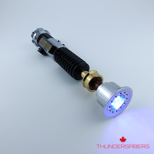 May include: A silver and black lightsaber with a black grip, gold accents, and a glowing blue emitter. The lightsaber has the text "THUNDERSABERS" and a maple leaf logo.