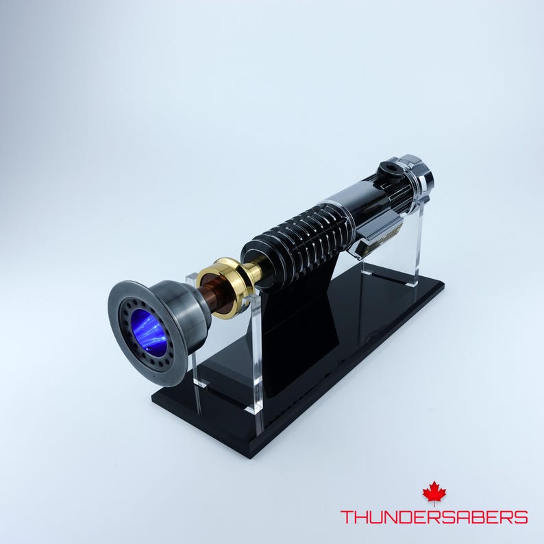 May include: A lightsaber with a blue blade, presented on a black stand. The hilt is a mix of silver, black, and gold. The text "THUNDERSABERS" is visible in the bottom right corner.