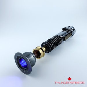 May include: A detailed lightsaber prop with a black, silver, and gold handle. The emitter end features a blue glowing plasma effect. The product is labeled with the text "THUNDERSABERS" and a maple leaf logo.