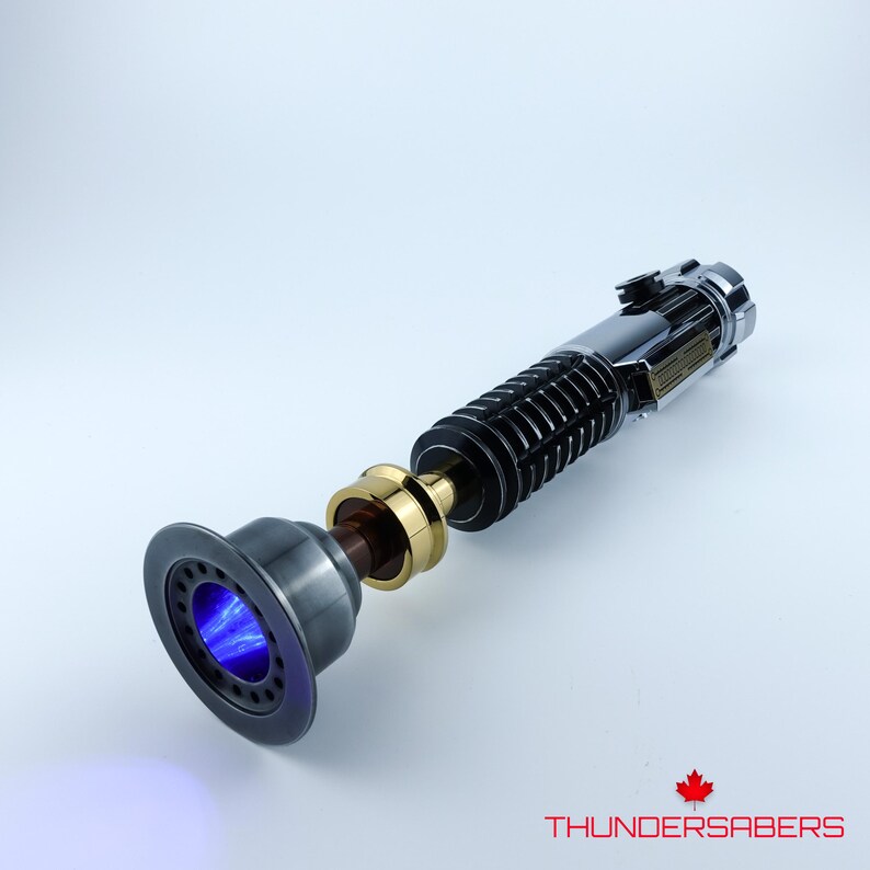May include: A detailed lightsaber prop with a black, silver, and gold handle. The emitter end features a blue glowing plasma effect. The product is labeled with the text "THUNDERSABERS" and a maple leaf logo.