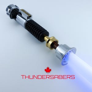 May include: A silver and black lightsaber with a blue glowing blade. The hilt features metallic accents and a ribbed grip. The text "THUNDERSABERS" is displayed below the lightsaber.