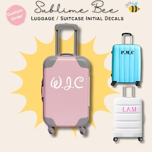 May include: Three suitcases with personalised initials. The suitcases are pink, blue and white. The pink suitcase has the initials W.J.C. in white cursive lettering. The blue suitcase has the initials P.M.C. in black lettering. The white suitcase has the initials L.A.M. in pink lettering.