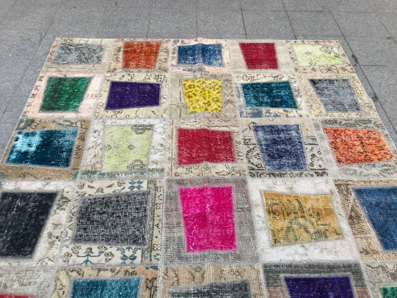 May include: A patchwork rug featuring a range of colours and patterns, including red, blue, green, yellow, and pink. The rug is crafted from various fabrics and textures, and has a distressed appearance.