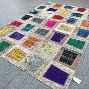 May include: A patchwork rug featuring a range of colours and patterns, including green, purple, yellow, and orange. The rug is crafted from various fabrics and textures, and has a distressed appearance.