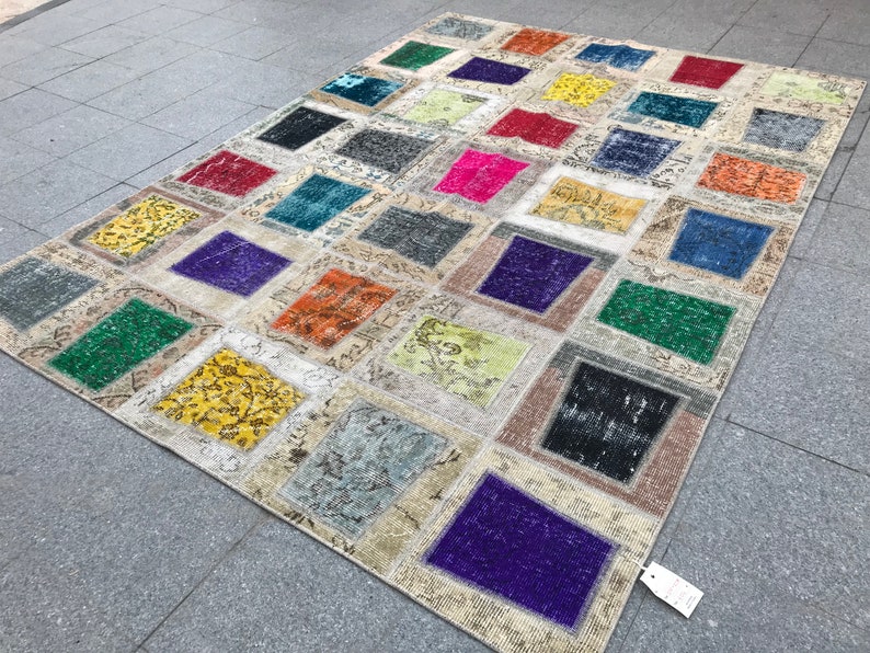 May include: A patchwork rug featuring a range of colours and patterns, including green, purple, yellow, and orange. The rug is crafted from various fabrics and textures, and has a distressed appearance.