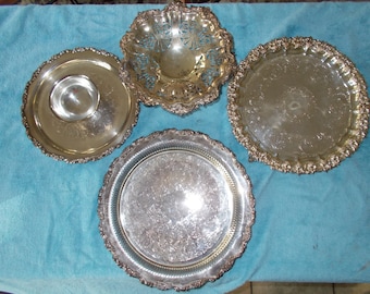 May include: Four silver serving trays with ornate designs. The trays are arranged on a blue surface.