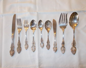 May include: A set of silver-plated cutlery, including a butter knife, a dinner fork, a salad fork, a teaspoon, a soup spoon, a butter spreader, a serving fork, and a serving spoon. The cutlery has an ornate, floral design.