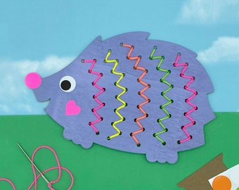 May include: Purple wooden hedgehog with a pink nose and eyes. The hedgehog has a heart on its chest and is decorated with colorful zig-zag stitching.