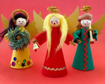 May include: Three handmade felt Christmas angels with gold wings and haloes. The angel in the center is wearing a red dress, the angel on the left is wearing a yellow dress, and the angel on the right is wearing a green dress.