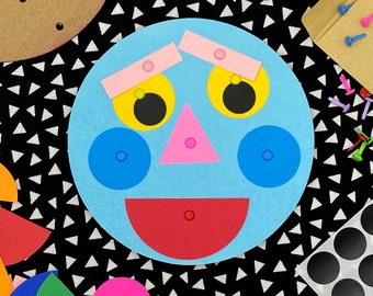 May include: A light blue circular face cutout featuring two yellow eyes with black pupils, two pink rectangular eyebrows, a pink triangular nose, two blue circular cheeks, and a red semi-circular mouth, all attached with small colorful metal fasteners.