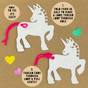 May include: Two white glitter unicorn shapes with pink yarn tails. Instructions for tying the yarn tails are included: "1. Fold yarn in half to make a loop; thread loop through hole" and "2. Thread ends through loop & pull gently".