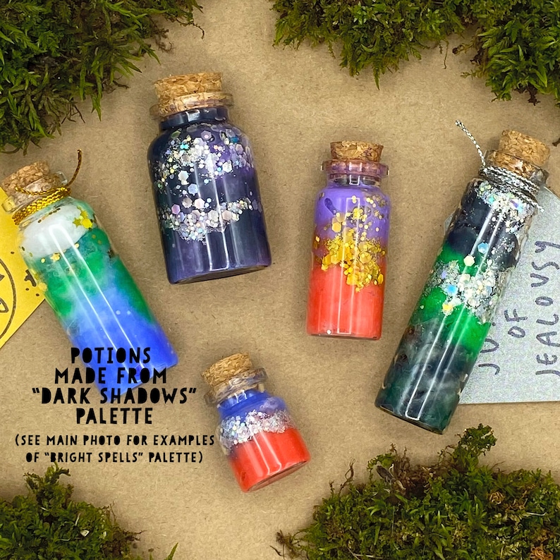 May include: Five small glass potion bottles with cork stoppers. The bottles contain colorful liquids and glitter. Text on the image reads "POTIONS MADE FROM DARK SHADOWS PALETTE" and "JUICE OF JEALOUSY".