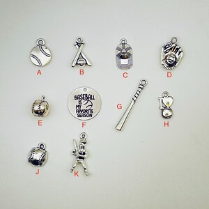 May include: A collection of silver-toned baseball-themed charms. The charms include a baseball, a baseball bat and ball, a baseball cap, a baseball glove, and a charm with the text "Baseball is my favorite season."
