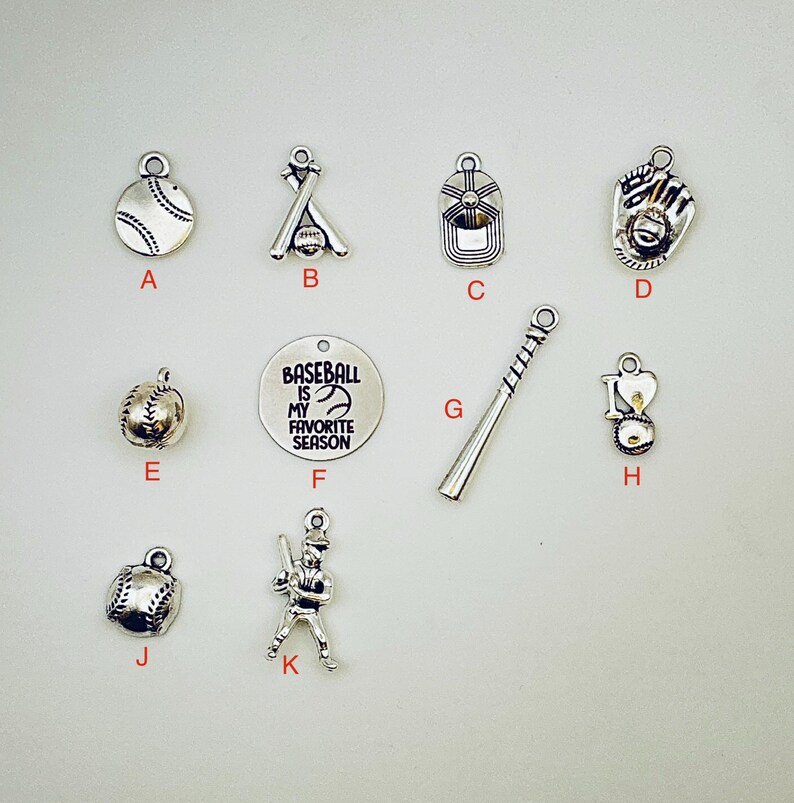 May include: A collection of silver-toned baseball-themed charms. The charms include a baseball, a baseball bat and ball, a baseball cap, a baseball glove, and a charm with the text "Baseball is my favorite season."