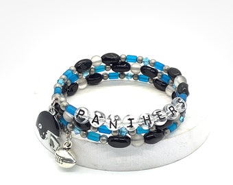 May include: A triple-strand beaded bracelet with black, white, and blue beads. The bracelet has a silver football charm and a black helmet charm. The beads spell out "PANTHERS".