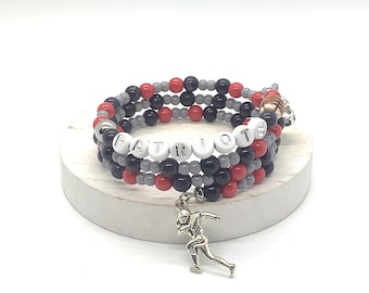 May include: A multi-strand wrap bracelet featuring red, black, and grey beads. The bracelet includes white letter beads spelling out PATRIOTS, a small brown football-shaped bead, and a silver-toned metal charm of a football player in motion.