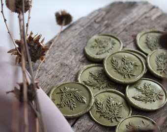May include: A close-up of nine olive green wax seals with a leafy design. The seals are arranged on a rustic wooden surface.