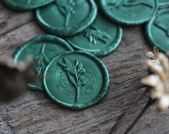 May include: A close-up of several green wax seals with a leaf design. The seals are on a wooden surface.