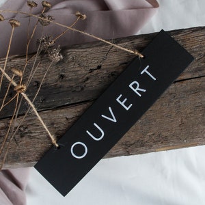 Peut inclure: Une pancarte noire avec l'inscription "OUVERT" en lettres blanches, suspendue à une ficelle sur une planche de bois vieillie.