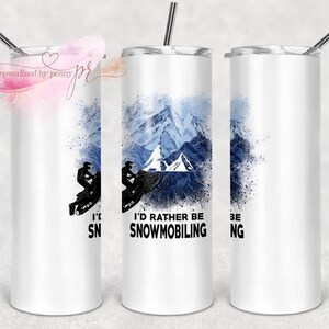 Peut inclure: Un gobelet en acier inoxydable blanc avec une scène de montagne aquarelle bleue et blanche et une silhouette d'une personne en motoneige. Le texte "I'd rather be snowmobiling" est imprimé sur le gobelet.