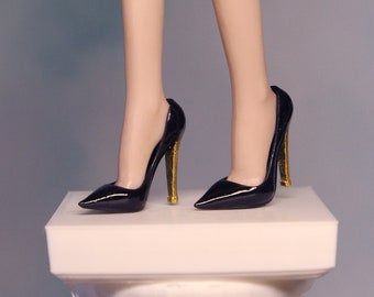 May include: A pair of black high-heeled shoes with gold accents on the heels. The shoes are pointed-toe and have a glossy finish.