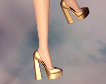 Puede incluir: Un par de tacones de plataforma dorados con un tacón alto y una plataforma gruesa. Los tacones están hechos de un material dorado brillante y tienen una punta puntiaguda.
