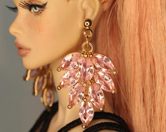Può includere: Una bambola con i capelli rosa raccolti in una coda di cavallo che indossa un paio di grandi orecchini di cristallo rosa con accenti dorati.