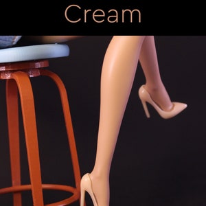 Puede incluir: Un par de tacones altos de color crema con punta puntiaguda. Los tacones los lleva una mu&ntilde;eca sentada en un taburete de madera con un asiento azul.