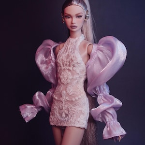 May include: A fashion doll with long, silver hair in a high ponytail. She wears a short, white lace dress and large, lavender-colored, puffy sleeves. The doll has detailed makeup and is wearing earrings. The background is a dark purple.