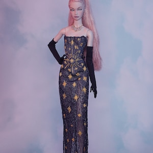 May include: A doll wearing a black gown with gold star embroidery and black gloves. The doll has pink hair and is wearing a necklace.
