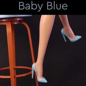Puede incluir: Un par de zapatos de tac&oacute;n alto de color azul claro con punta. Los zapatos son usados por una mu&ntilde;eca sentada en un taburete rojo. El texto "Baby Blue" se muestra sobre el taburete.