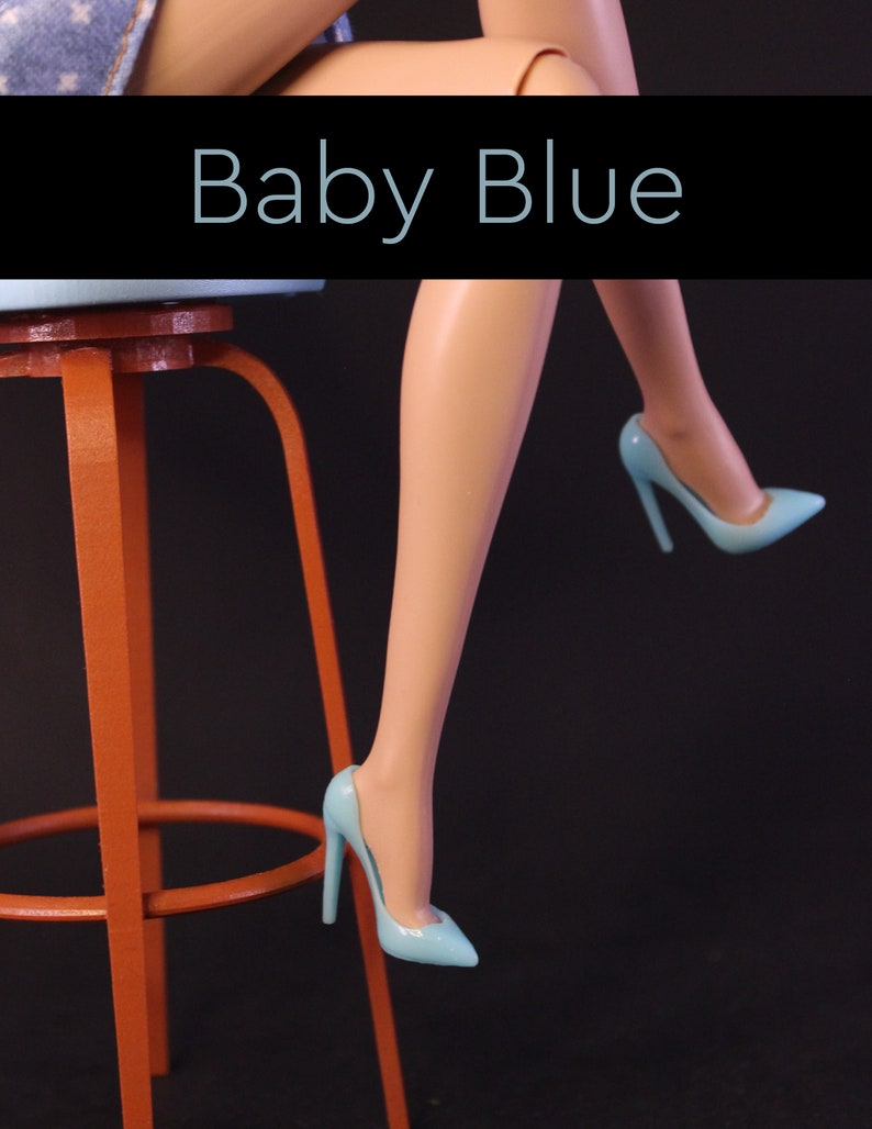 Puede incluir: Un par de zapatos de tac&oacute;n alto de color azul claro con punta. Los zapatos son usados por una mu&ntilde;eca sentada en un taburete rojo. El texto "Baby Blue" se muestra sobre el taburete.