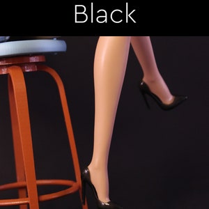 Puede incluir: Un par de zapatos negros de tac&oacute;n alto con punta. Los zapatos son usados por una mu&ntilde;eca sentada en un taburete.