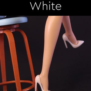 Puede incluir: Un par de zapatos blancos de tac&oacute;n alto con punta puntiaguda. Los zapatos son usados por una mu&ntilde;eca sentada en un taburete de madera.