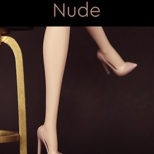 Puede incluir: Un par de tacones altos de color nude con punta. Los tacones est&aacute;n sobre un fondo oscuro.