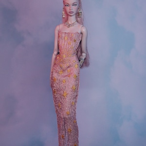 May include: A pink and gold sequined gown with a star pattern. The gown has a strapless bodice and a flowing skirt. The doll is wearing gold earrings and a gold necklace.
