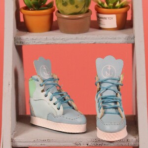 May include: A pair of blue high-top sneakers with white soles and green accents. The sneakers have an anchor logo on the side and blue laces.