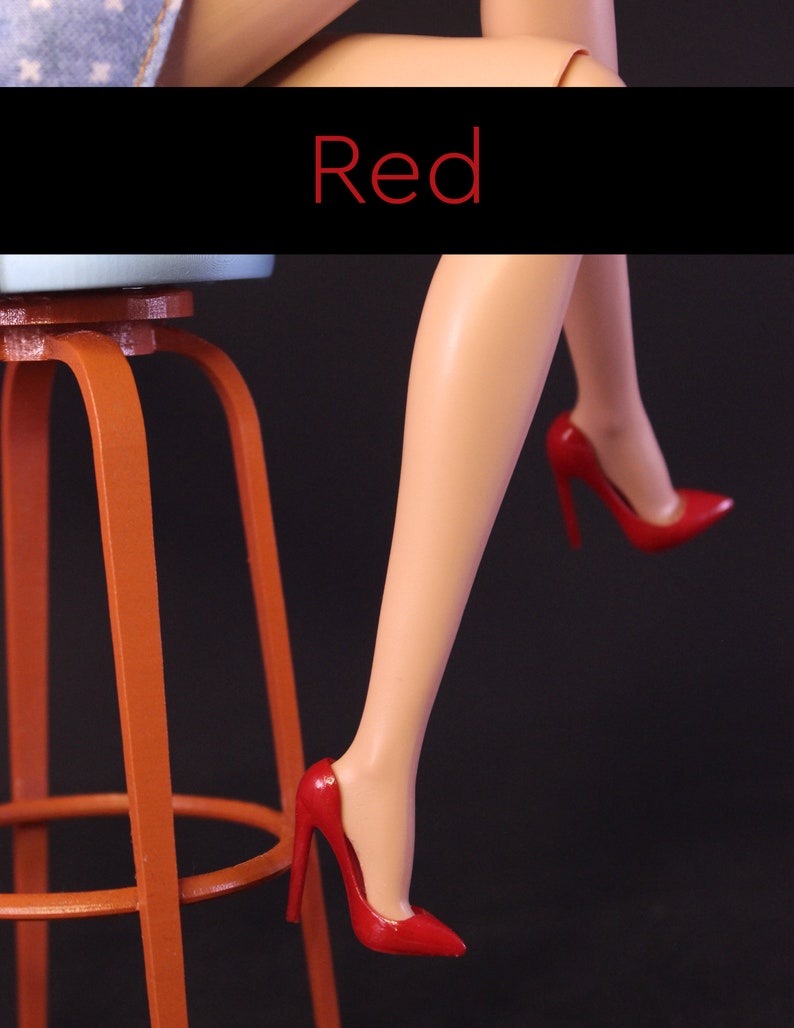 Puede incluir: Un par de zapatos de tac&oacute;n alto rojos con punta. Los zapatos son usados por una mu&ntilde;eca sentada en un taburete de madera.