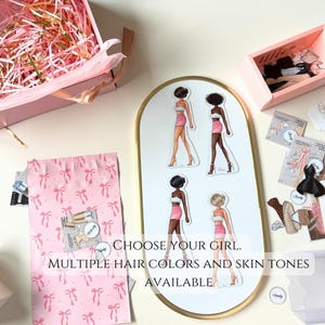 May include: A set of paper dolls with different hair and skin tones. The dolls are wearing pink skirts and white tops. The text on the image reads "Choose your girl. Multiple hair colors and skin tones available."