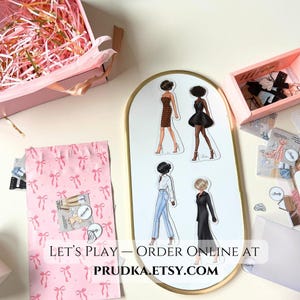 May include: A set of four paper doll cutouts featuring women in different outfits. The dolls are on a white background with a gold oval frame. The text "Let's Play - Order Online At PRUDKA.ETSY.COM" is at the bottom of the frame.