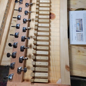 May include: A wooden soap cutter featuring a series of thin metal wires tensioned by chrome tuning pegs mounted on a wooden block. The device includes a set of wooden spacers and a printed instruction card titled Congratulations on the purchase of your new soap cutter, showing 10-Bar and 20-Bar configurations.