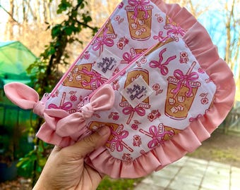May include: Two pink and white cosmetic bags with a repeating pattern of iced coffee drinks, bows, and flowers. The bags have pink ruffles and bows. The text "Baby Elephant" is on a small label on each bag.