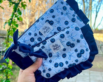 May include: Two matching blue and white zippered pouches with a blueberry and bow pattern. The pouches have a dark blue ruffle trim and a dark blue bow. The text "Baby Rybart" is on a small white tag on each pouch.