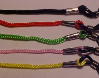 May include: Five eyeglass retainers with different colored cords. The cords are black, red, green, pink, and yellow. Each retainer has a silver metal slider and black plastic ends.